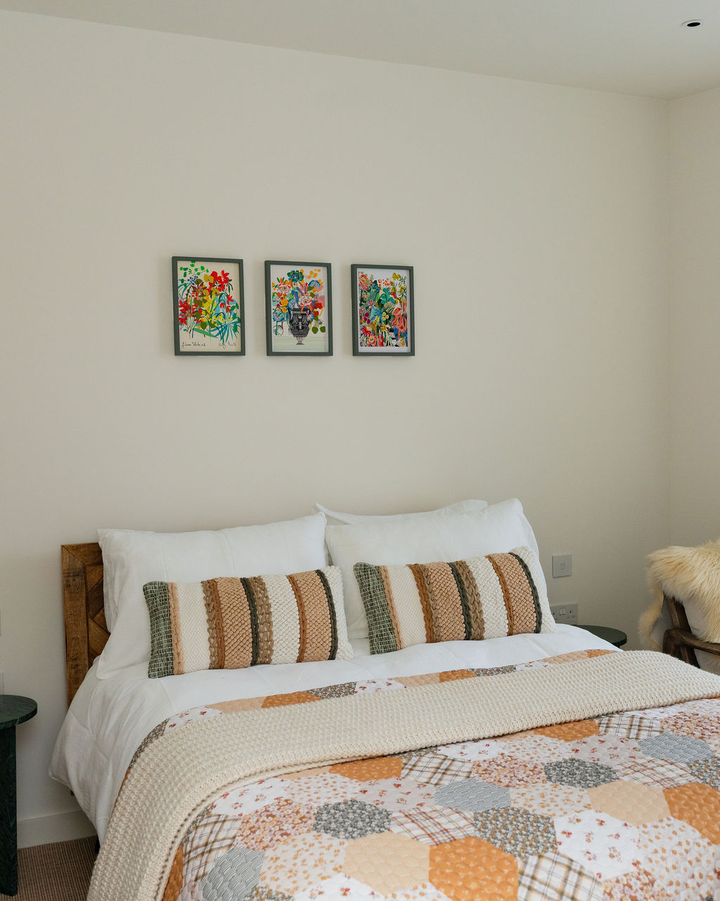 Double bed with patchwork quilt and three framed botanical prints