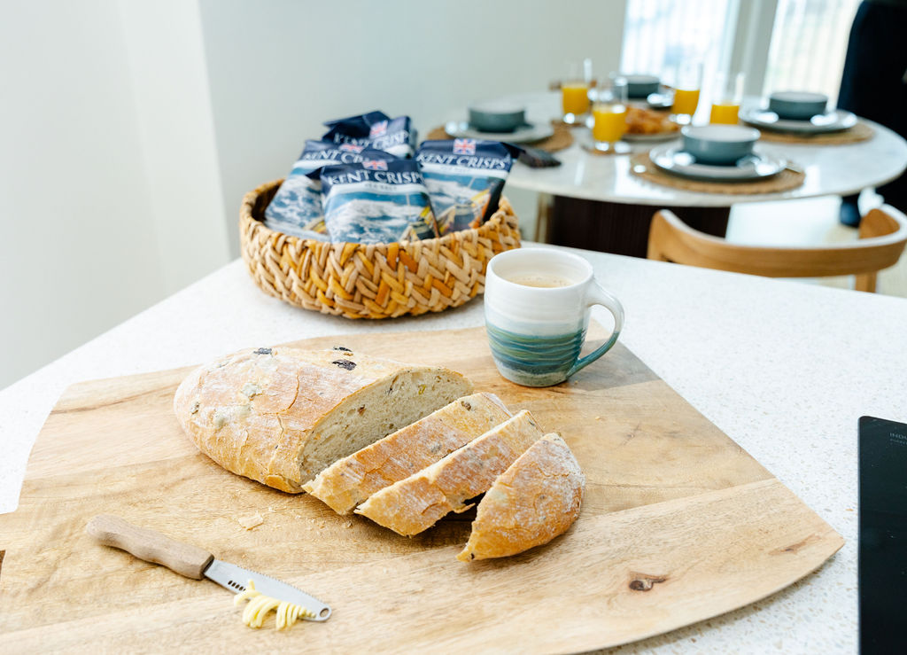 Sliced sourdough and coffee on a chopping board with breakfast laid in the background