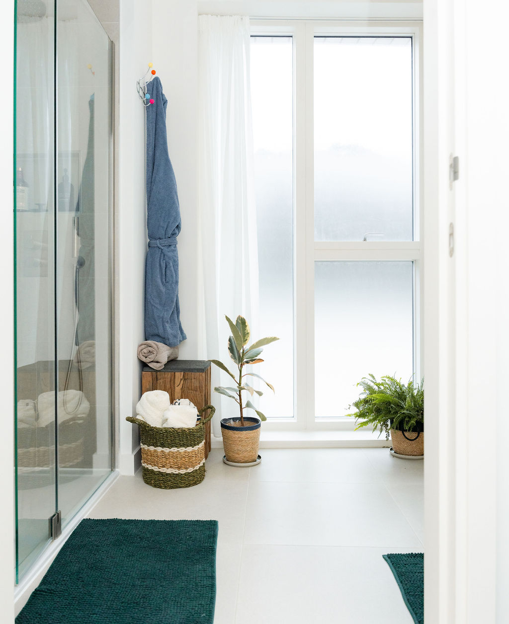 Bright bathroom hallway with robe, towels and indoor plants by a tall window